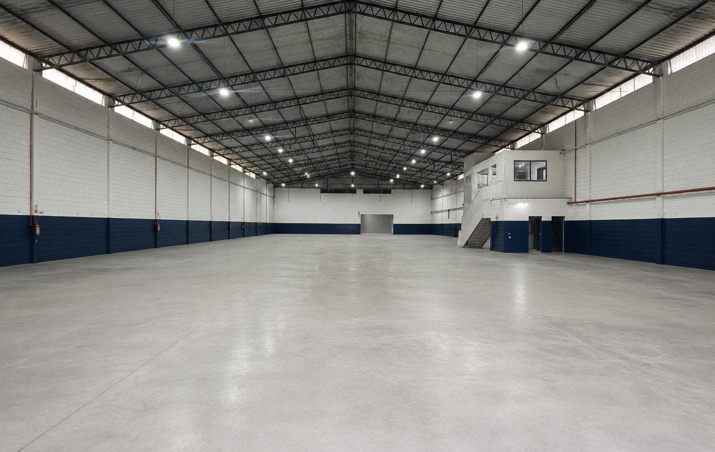 Interior do galpão, piso de concreto polido e tesouras metálicas